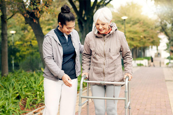 Two women walking down a path with a walker, supporting each other while enjoying a stroll together.