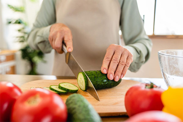 Woman preparing food, slicing a cucumber on a cutting board.